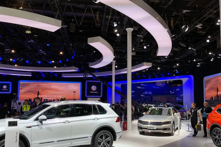 白色 Tiguan 与白色 Passat 停在弧形白色天花带之下，身后是蓝色灯光的墙面与屏幕