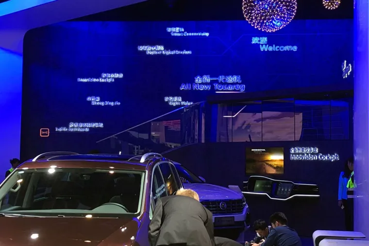 蓝色灯光的特色墙上有中英文发光标语，包括 All New Touareg，前方停着一辆棕色 SUV