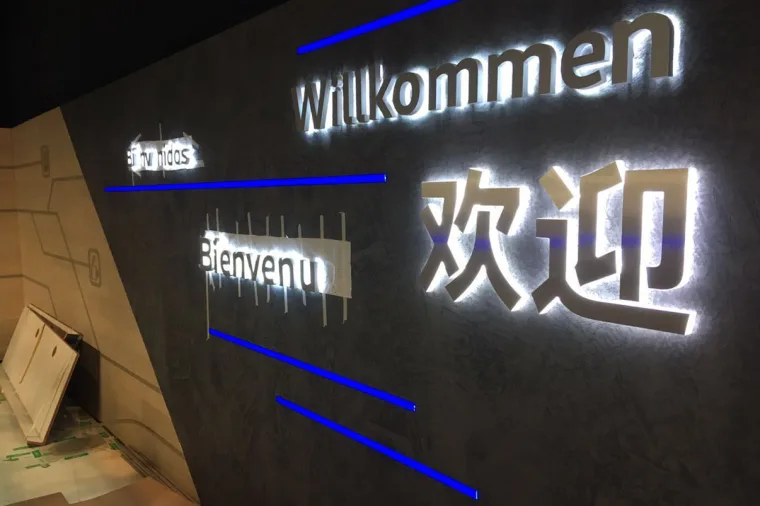 欢迎墙特写，Willkommen、Bienvenue 与中文问候语以灯光勾勒，蓝色像素灯带在其间穿行