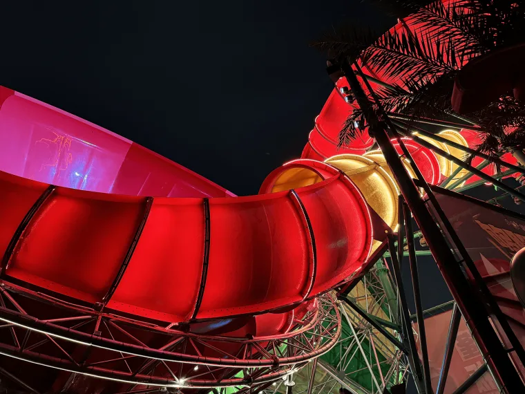A red flume curving steeply downward in close up, palm fronds silhouetted against green light below