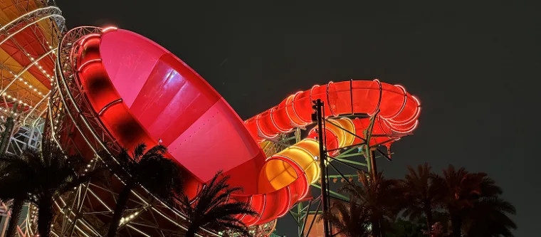 Red and orange funnel slides glowing against a black sky, silhouetted palm fronds across the foreground