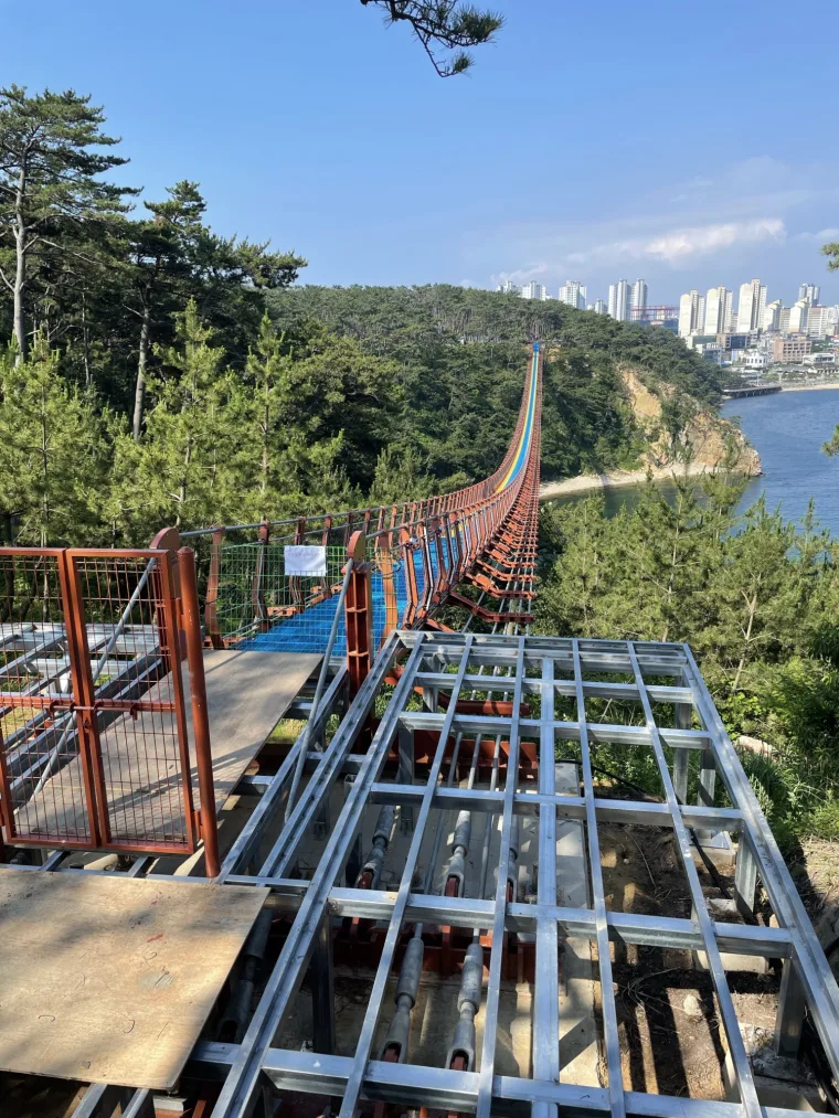 施工中登陆段的钢制桥面框架，红色桥身横跨海湾伸向城市天际线
