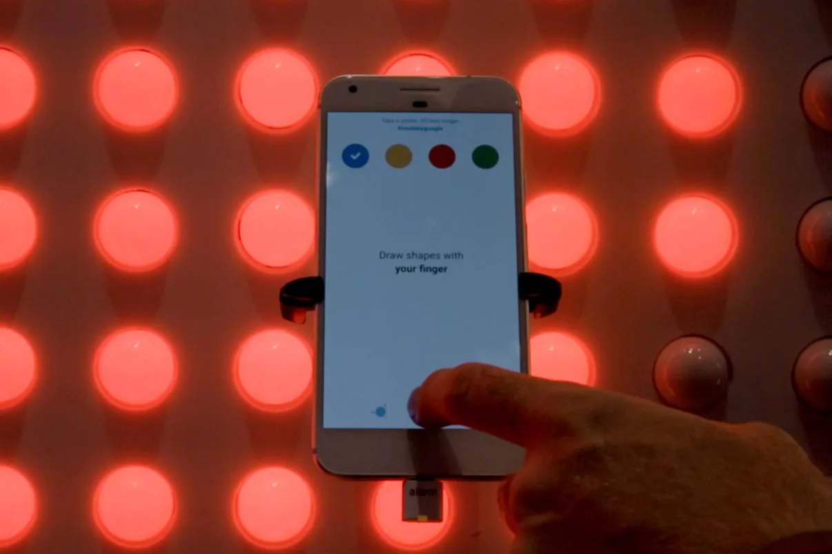 一部 Google Pixel 手机举在亮起红光的像素点前,屏幕上的应用提示用手指绘制图形
