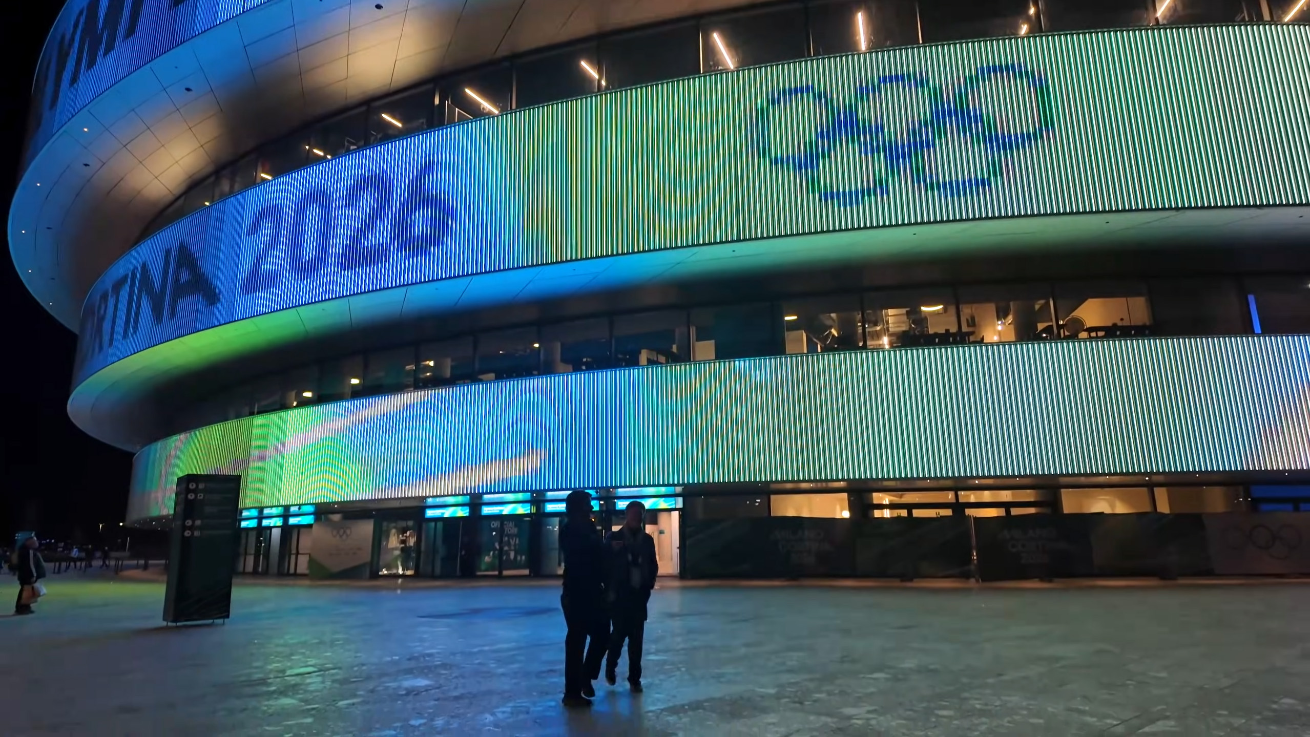 Arena Milano at night, its media façade lit with the Olympic rings and Milano Cortina 2026 branding