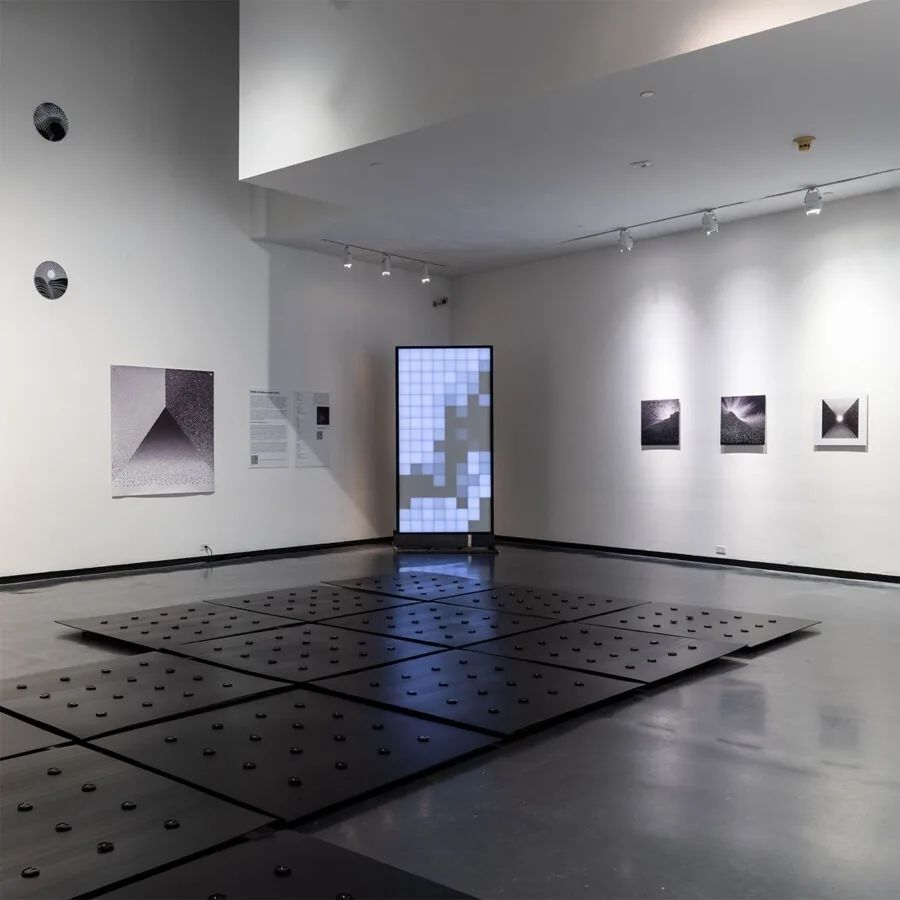 展厅一角，方碑在墙面版画之间亮起，深色地板与其上的黑点占据前景