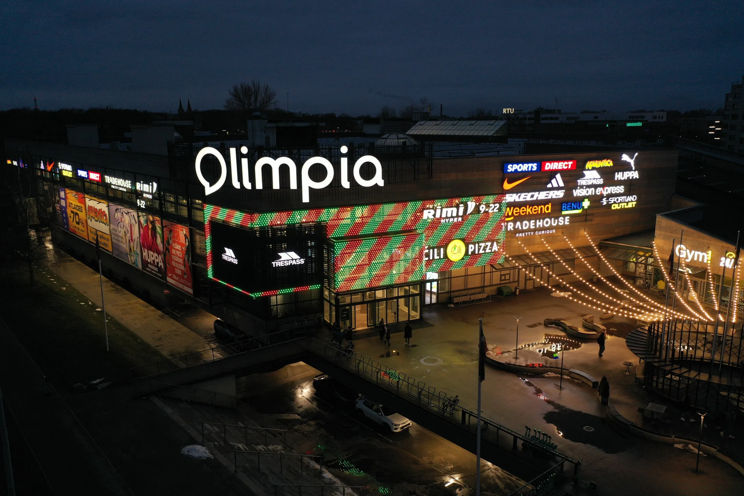 The facade running a green and red chevron pattern at dusk, retail signage lit along the frontage