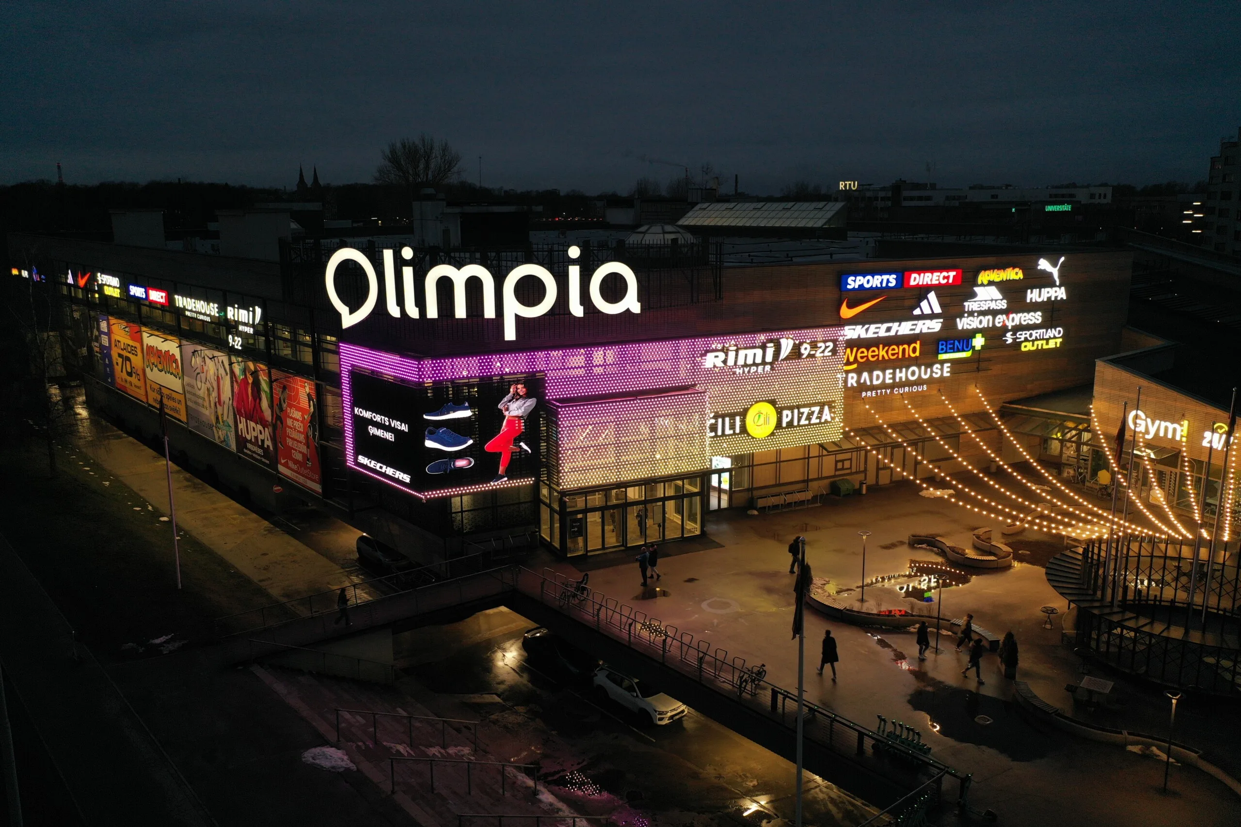 A figure rendered in magenta and purple across the pixel facade, the plaza dark and wet below