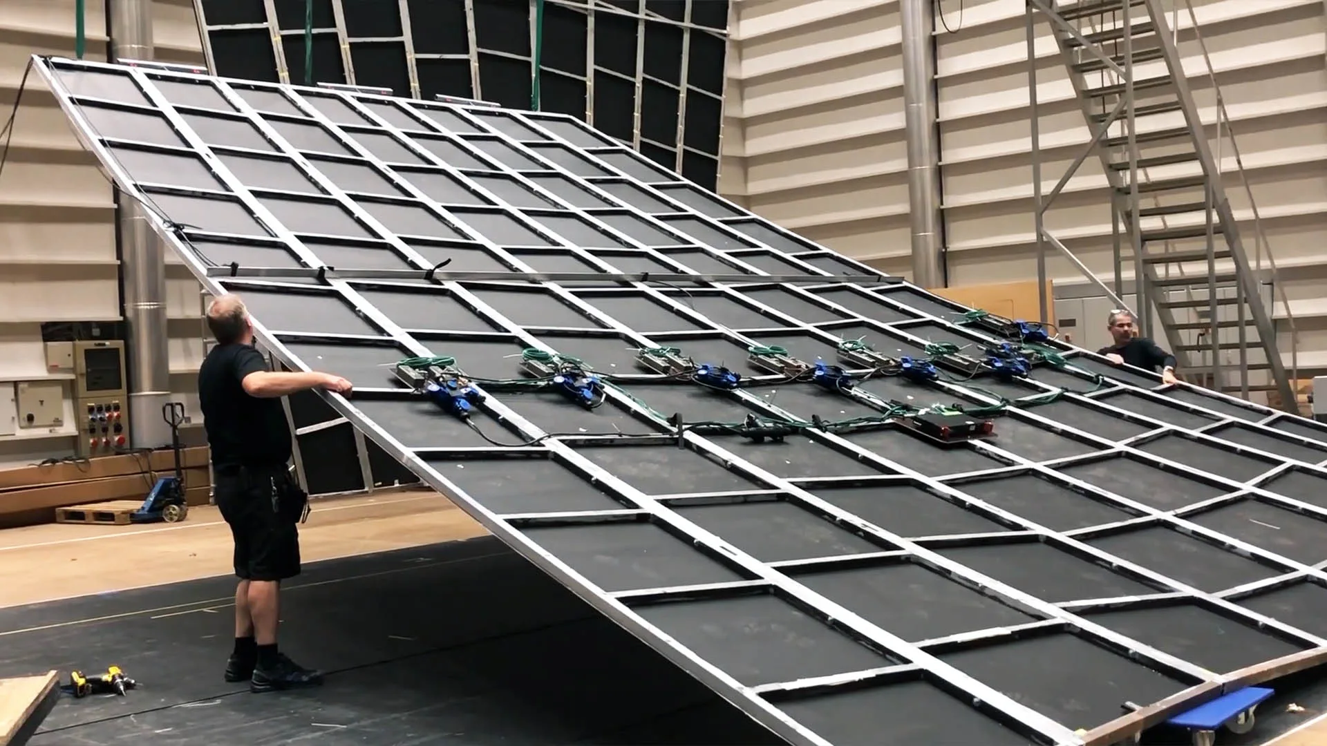 两名工作人员将一副大型钢制网格框架从地面立起,中继器已经安装在框架的横梁上