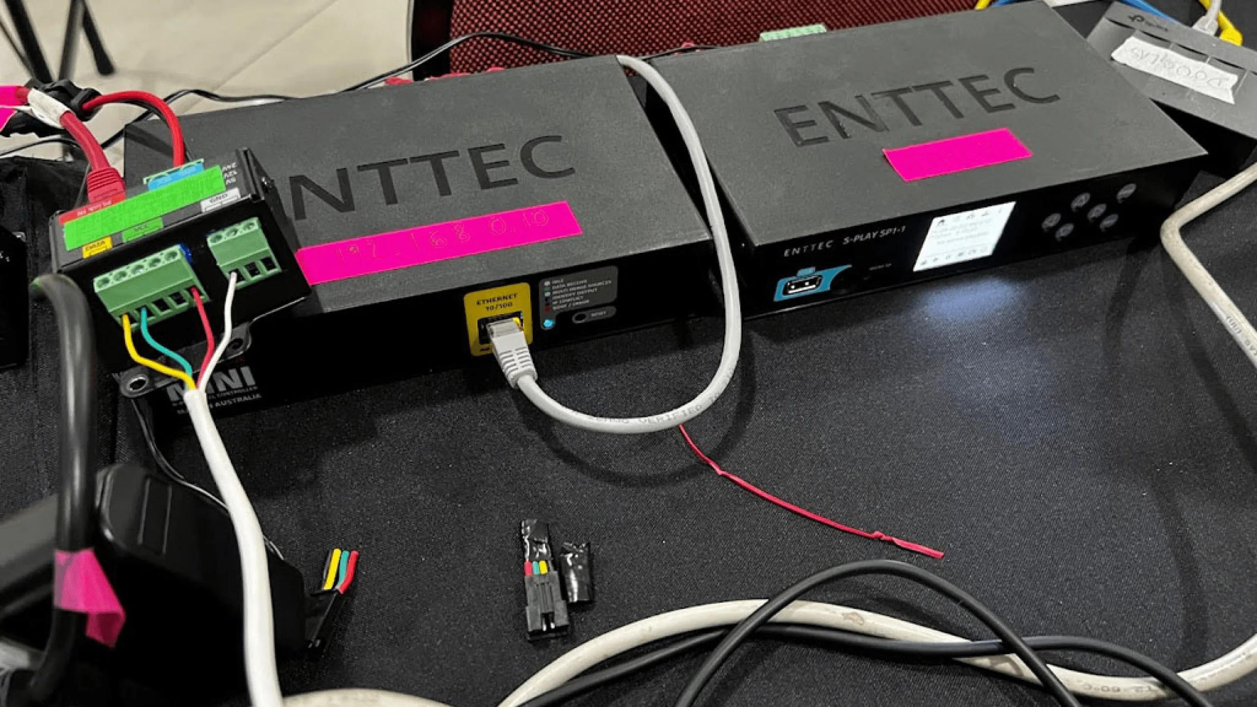 桌面上两台贴着粉色标签的黑色 ENTTEC 控制器，网线与红黑电源线从上面延伸出去