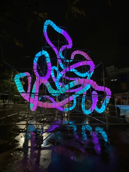 夜间脚手架上的蓝色、紫色与青色光环，色彩倒映在湿漉漉的地面上