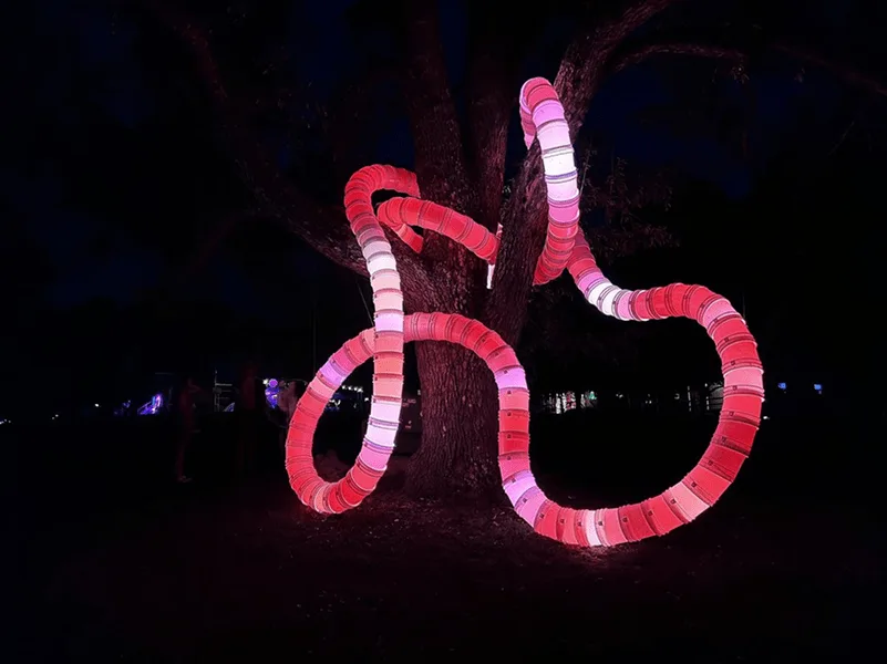 黑色夜景中，缠绕树木的管体亮起深红与粉色，树干在光晕中被勾勒出来