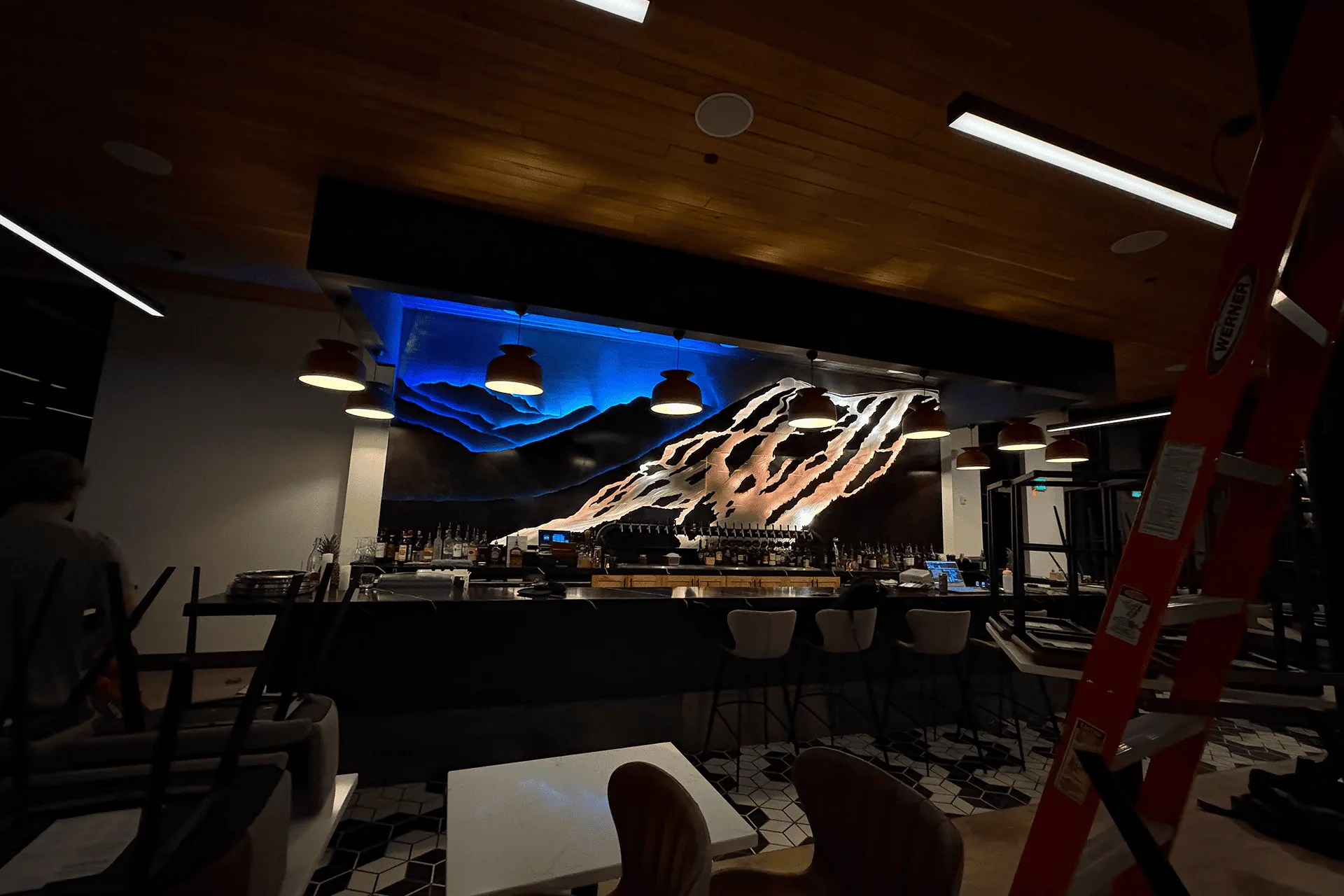 The sculpture lit blue during fit-out, with a ladder and unfinished dining room around it