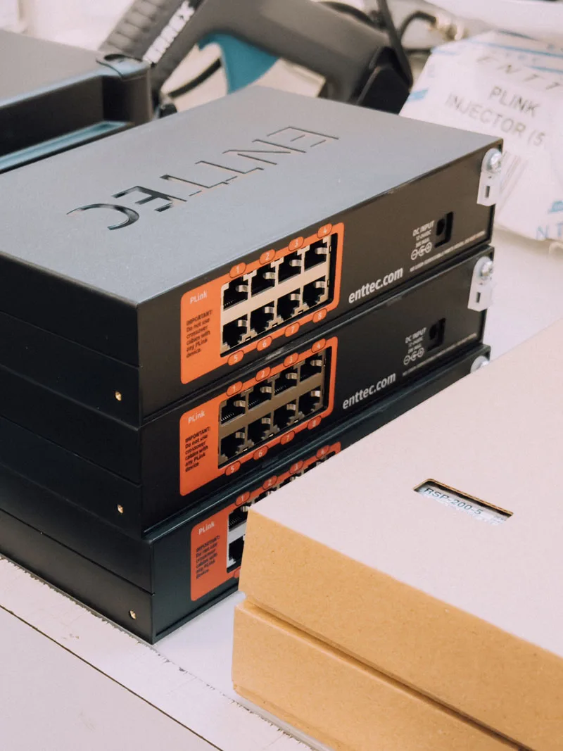 工作台上的两台黑色 ENTTEC 控制器,橙色标识的输出端口朝外,后方堆放着 PLink Injector 的包装箱