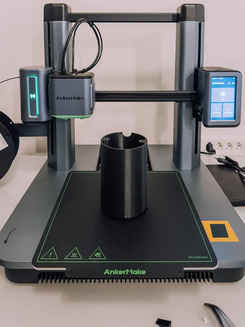 桌面 3D 打印机正在打印其中一个黑色圆柱形灯罩