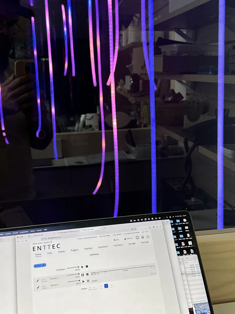 粉色与紫色灯绳映在深色屏幕上,下方的笔记本电脑打开着 ENTTEC 配置页面