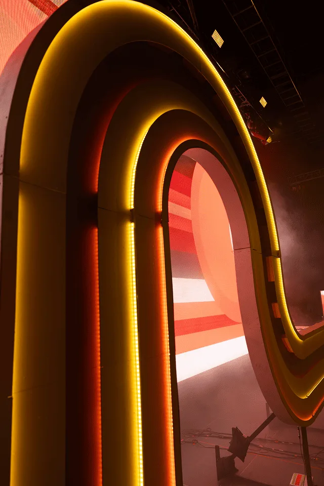 Close-up of the arch, layered yellow and orange neon tubes curving through haze above the stage floor