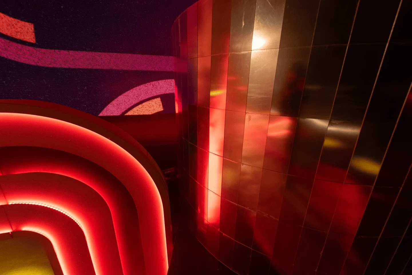 The mirror-tiled DJ booth catching red light off the arch, its panels breaking the glow into fragments