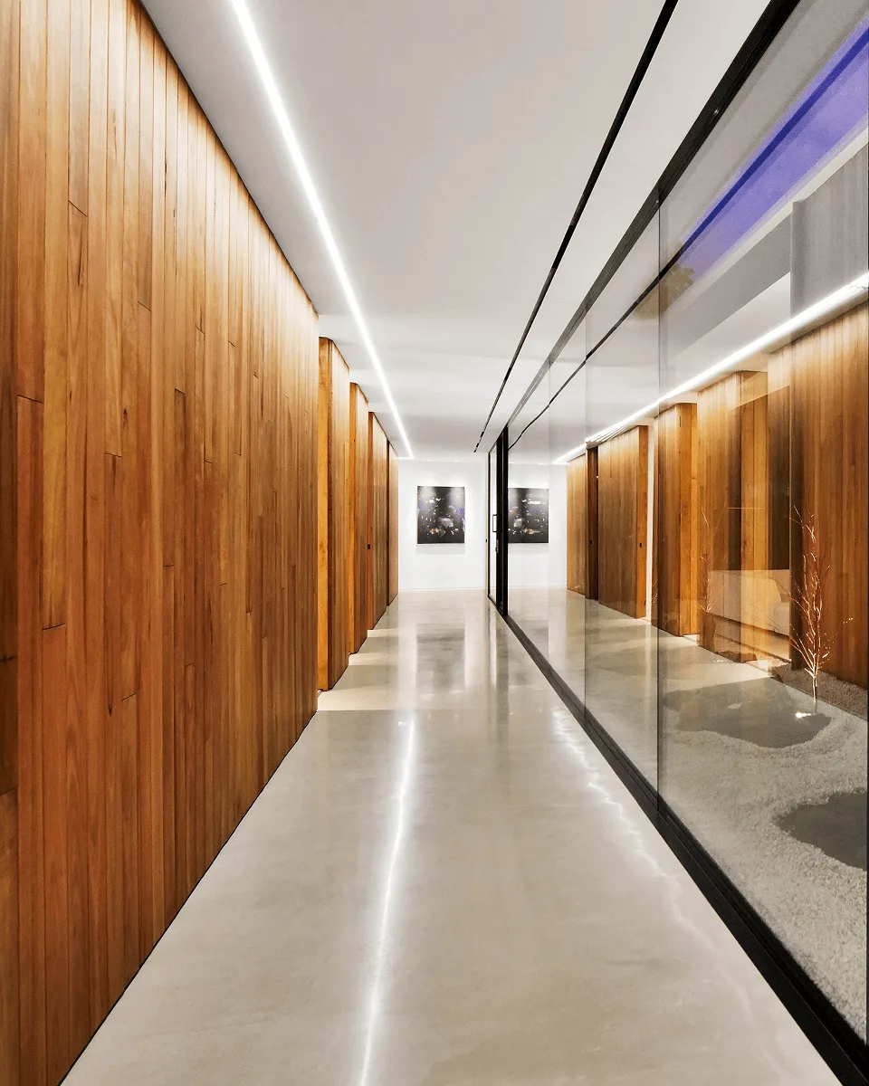 Looking down the length of the corridor, polished concrete floor reflecting the ceiling strip, framed prints on the far wall