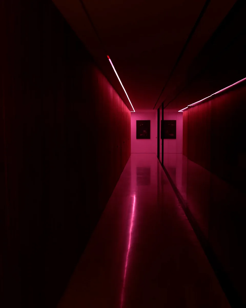 The corridor washed deep magenta at night, two framed prints glowing at the far end