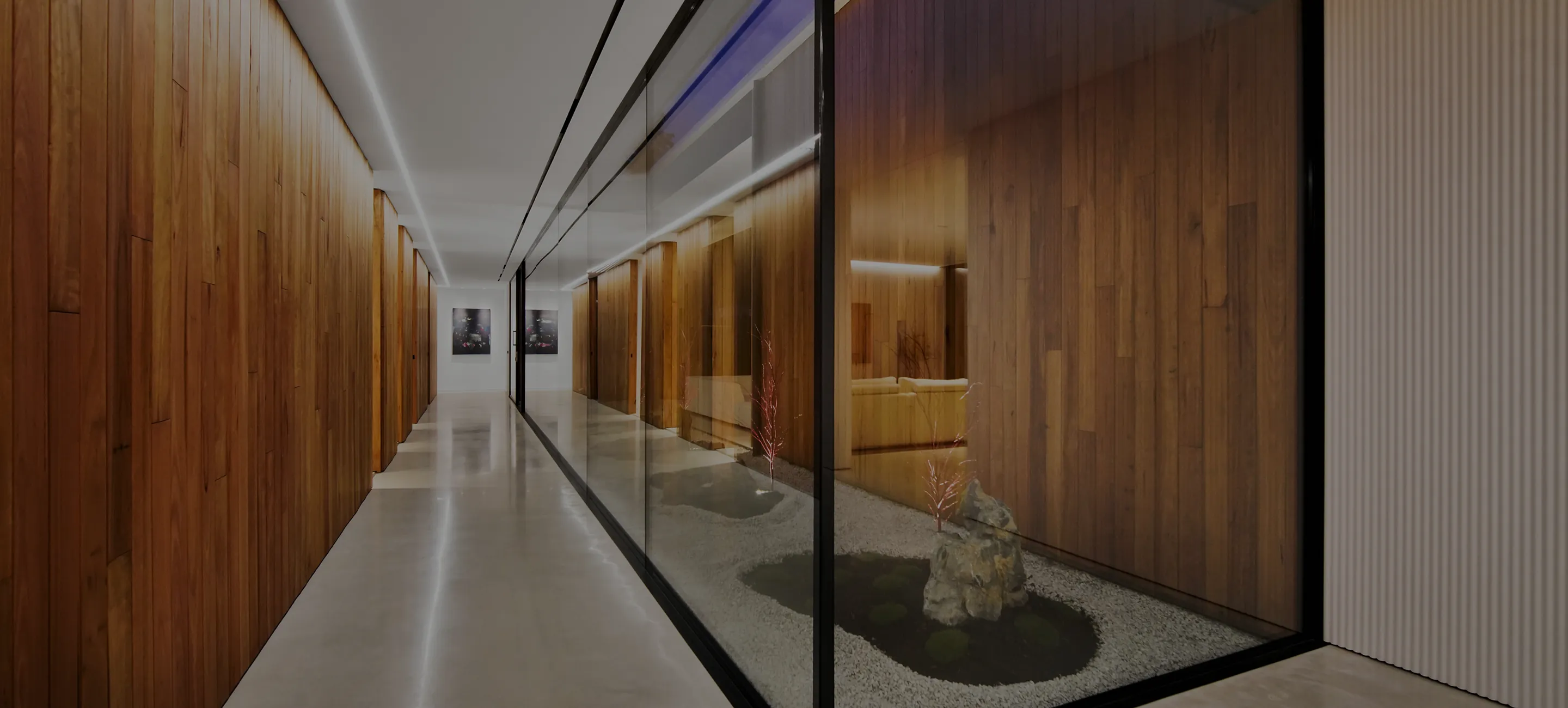 The 25-metre hallway of Zanetto House in daylight, timber walls, a glazed rock garden alongside and a continuous LED line in the ceiling